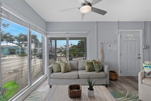 Ein modernes Wohnzimmer mit einem grauen Sofa, einem Deckenventilator und Blick durch große Schiebeglastüren.