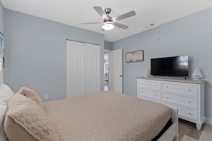 Quarto com cama, televisão, penteadeira e ventoinha no teto.