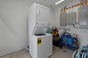 Een wasserij met een voorlader wasmachine en droger, een kar met schoonmaakmiddelen en elektrische panelen aan de muur.