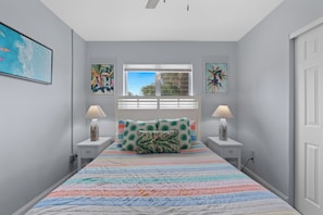 Quarto com cama, duas mesas de cabeceira, janela com persianas e decoração na parede.