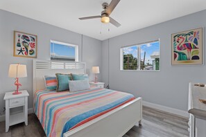 A bedroom with a bed, two bedside tables, a ceiling fan, a window with blinds, and artwork on the walls. - 🐾 Dune Your Thing B | Pet Friendly FMB | Heated Pool + Beach Access (Fort Myers Beach)