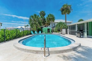 A swimming pool with a metal safety rail, surrounded by a fence, with palm trees and a building in the background. - 🐾 Dune Your Thing B | Pet Friendly FMB | Heated Pool + Beach Access (Fort Myers Beach)