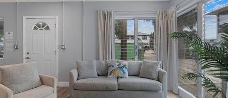 A living room with a sofa, a coffee table, and a large window with curtains.