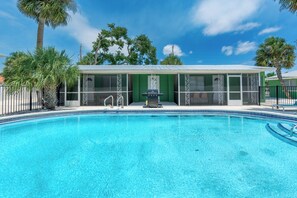 Ein Schwimmbad mit überdachtem Bereich, Palmen und blauem Himmel.