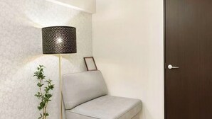 Una habitació moderna amb un sofà gris, una làmpada de peu, una planta en test i una porta de fusta fosca.