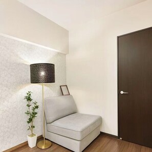 Een moderne kamer met een grijze bank, een vloerlamp, een potplant en een donkerhouten deur.