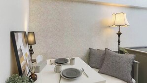 Zona de menjador amb taula per a dues persones, un rellotge de paret, una làmpada i coixinets amb dibuixos.