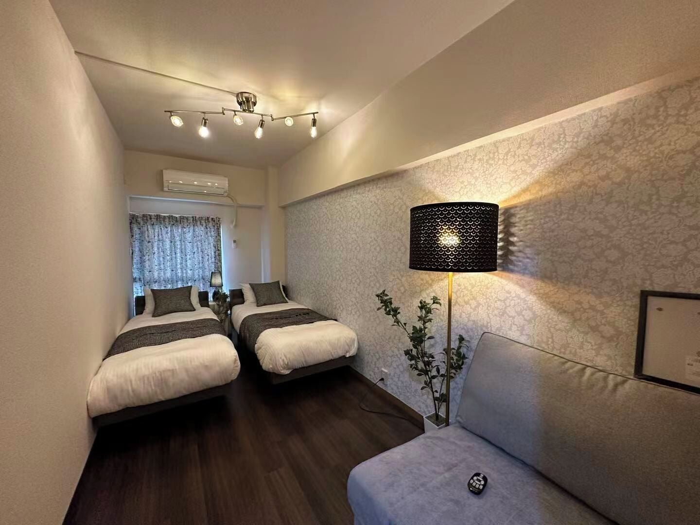 Une chambre d’hôtel avec deux lits, un canapé, une lampe et une fenêtre avec des rideaux.