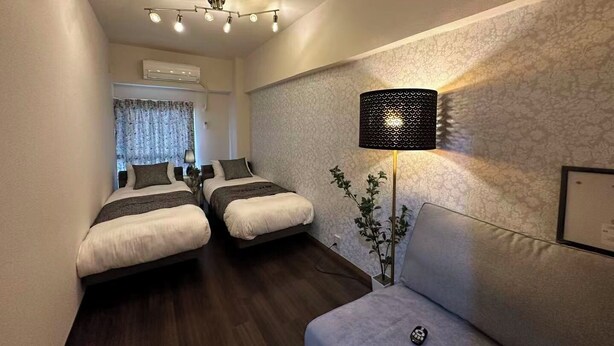 Habitació d'hotel amb dos llits, un sofà, una làmpada i una finestra amb cortines.