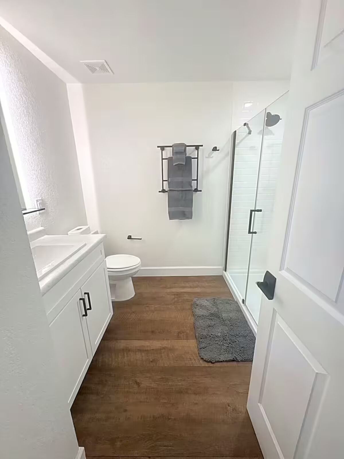 Un baño con inodoro, perchero para toallas, ducha y suelo de madera.