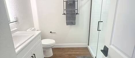 Un baño con inodoro, perchero para toallas, ducha y suelo de madera.