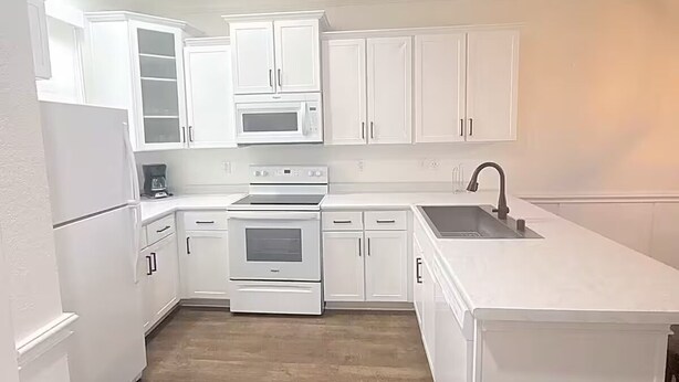 A modern kitchen with white cabinetry, a microwave, an oven, and a sink.