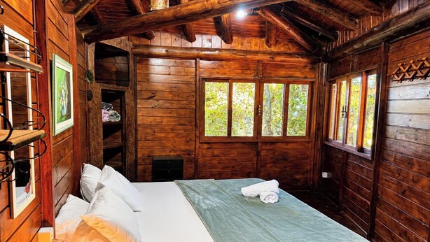 Quarto de cabana de madeira com cama, janela e prateleira com sapatos.