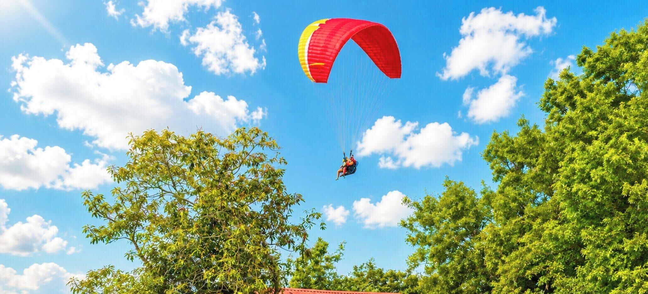 Una persona practica parapente con un paracaídas rojo y amarillo sobre una zona arbolada.