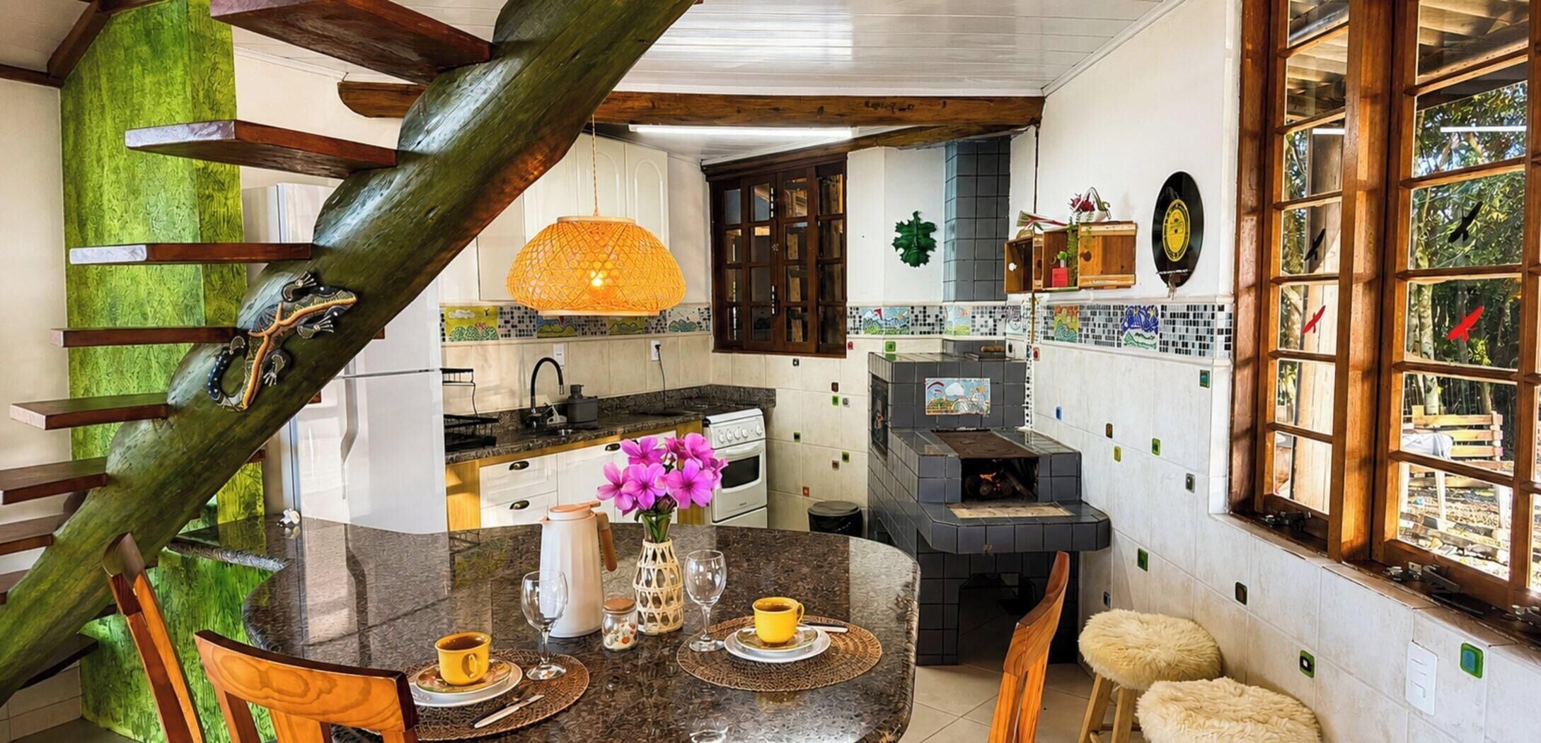 A kitchen with a dining area, wooden staircase, and a view of the outdoors.