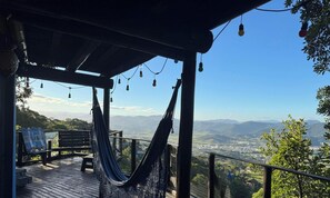 Una cadira d'hamaca sota una pergola de fusta amb llums de cadena, amb vista a una vall i muntanyes llunyanes.