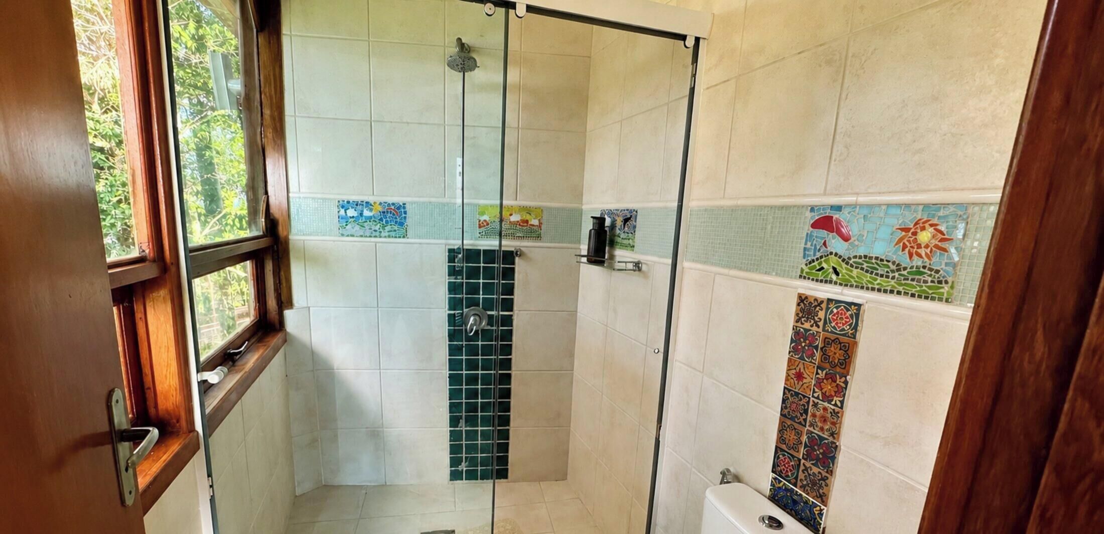 Ducha con puerta de cristal, paredes enlosadas y ventana.