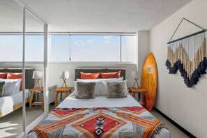 Een moderne hotelkamer met een groot bed, twee nachtkastjes, een macramé wanddecoratie en een surfboard decoratie.