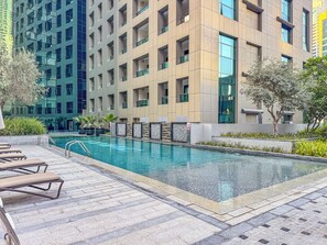 A swimming pool with lounge chairs, surrounded by modern buildings and greenery. - Prime 3Bed APT Near Dubai Canal & Burj Khalifa (Dubai)