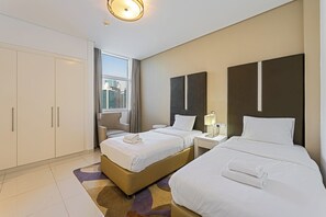 Ein Hotelzimmer mit zwei Betten, einem Schreibtisch, einem Stuhl, einem Fenster mit Blick auf die Stadt und einem großen Kleiderschrank.