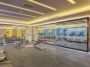 Ein Fitnessraum mit Trainingsgeräten, einem Wasserspender und einer Spiegelwand.