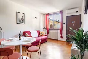Una habitación con una mesa de comedor, sillas, un sofá, un radiador, una puerta y una planta.