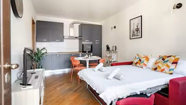Un dormitorio con cama, escritorio, silla y una pequeña cocina americana.