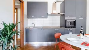 Una cocina moderna con armarios grises, una encimera blanca y una mesa de comedor redonda con sillas rojas.