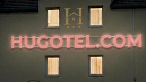Een gebouw met een bord waarop 'HUGOTEL.COM' staat en een logo erboven.