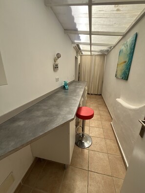 Une cuisine étroite avec un tabouret de bar, une fenêtre avec des rideaux et un tableau accroché au mur.