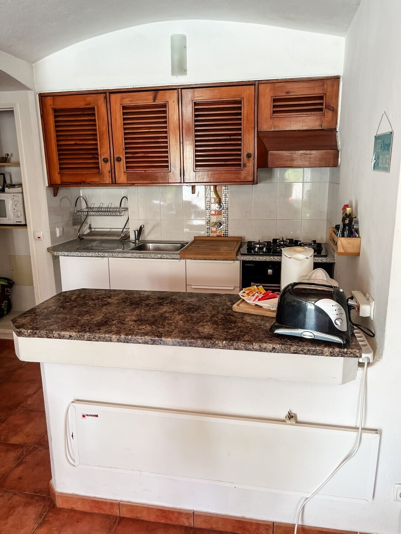 A compact kitchen with wooden cabinets, a granite countertop, a built-in oven, and a toaster.