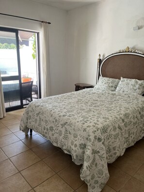 A bedroom with a bed, a nightstand, a chair, and a view through a sliding door to an outdoor area.