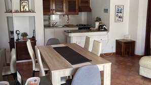 A modern kitchen with wooden cabinets, a dining area with a wooden table and chairs, and a hanging light fixture. - Private Pool • 8-Min Walk to Praia da Oura Beach • Prime Albufeira Location (Albufeira)