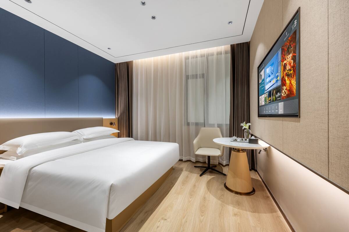 Una habitación de hotel con cama, escritorio, silla, televisor y ventana con cortinas.