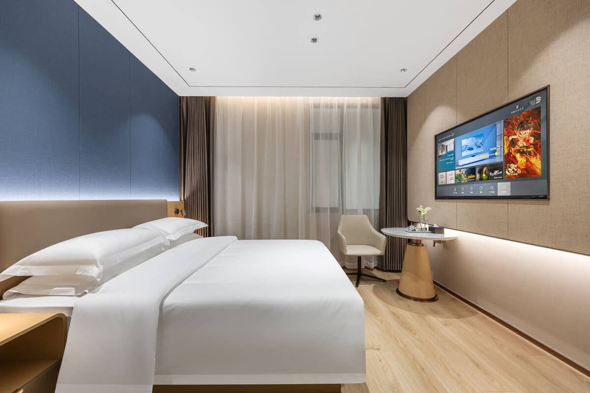 Habitación de hotel con cama, una mesita, una silla, televisor y cortina.