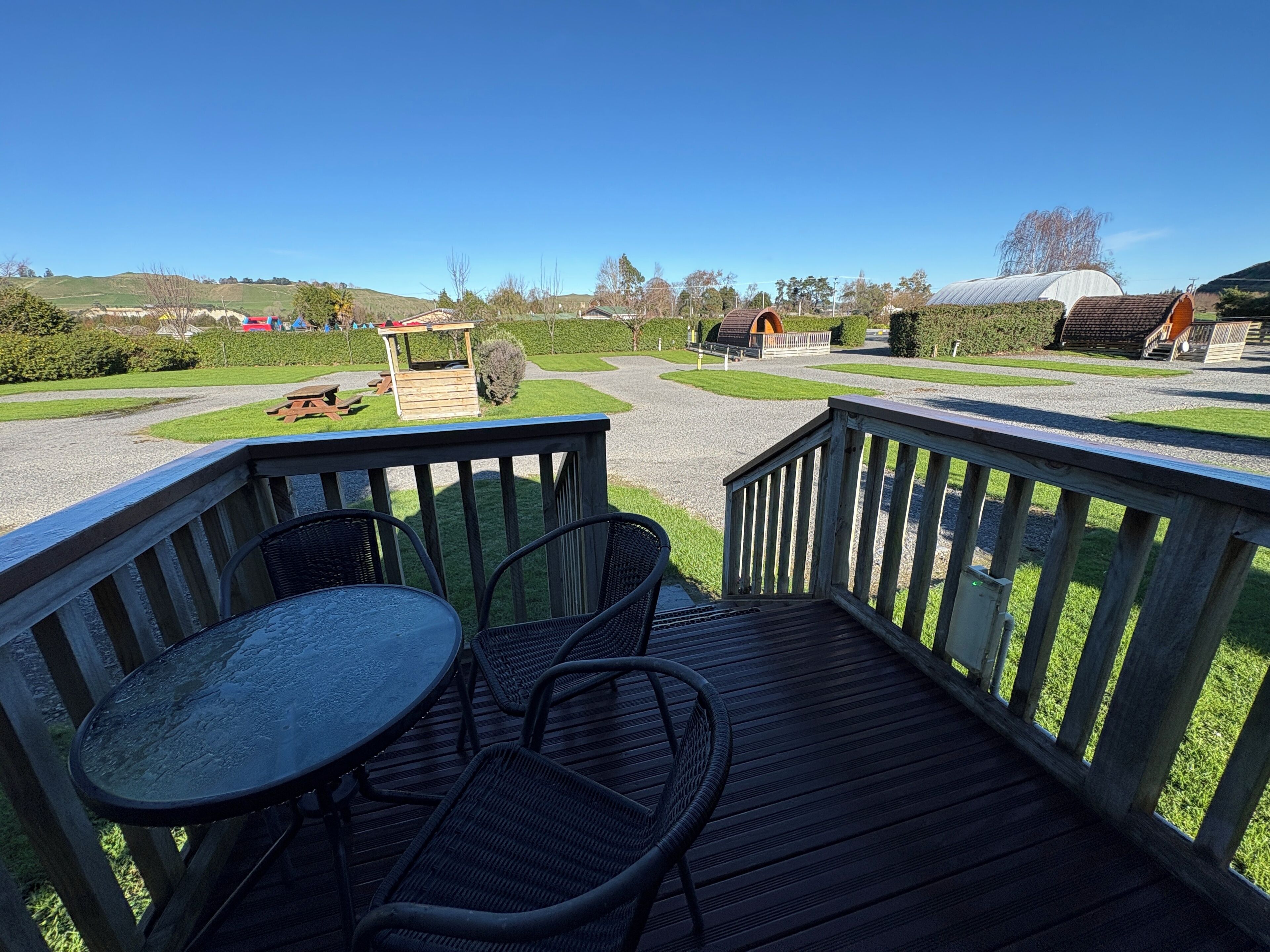 A wooden deck with a table and chairs, a picnic table, and a gazebo in a landscaped area with a clear sky.