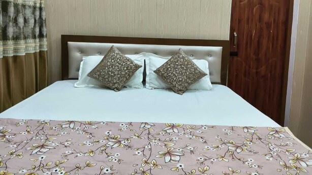 A bed with a floral bedspread, two patterned pillows, and a wooden headboard. - Amrit Niwas (Ayodhya)