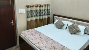 A bedroom with a bed, curtains, a door, and a wall socket. - Amrit Niwas (Ayodhya)