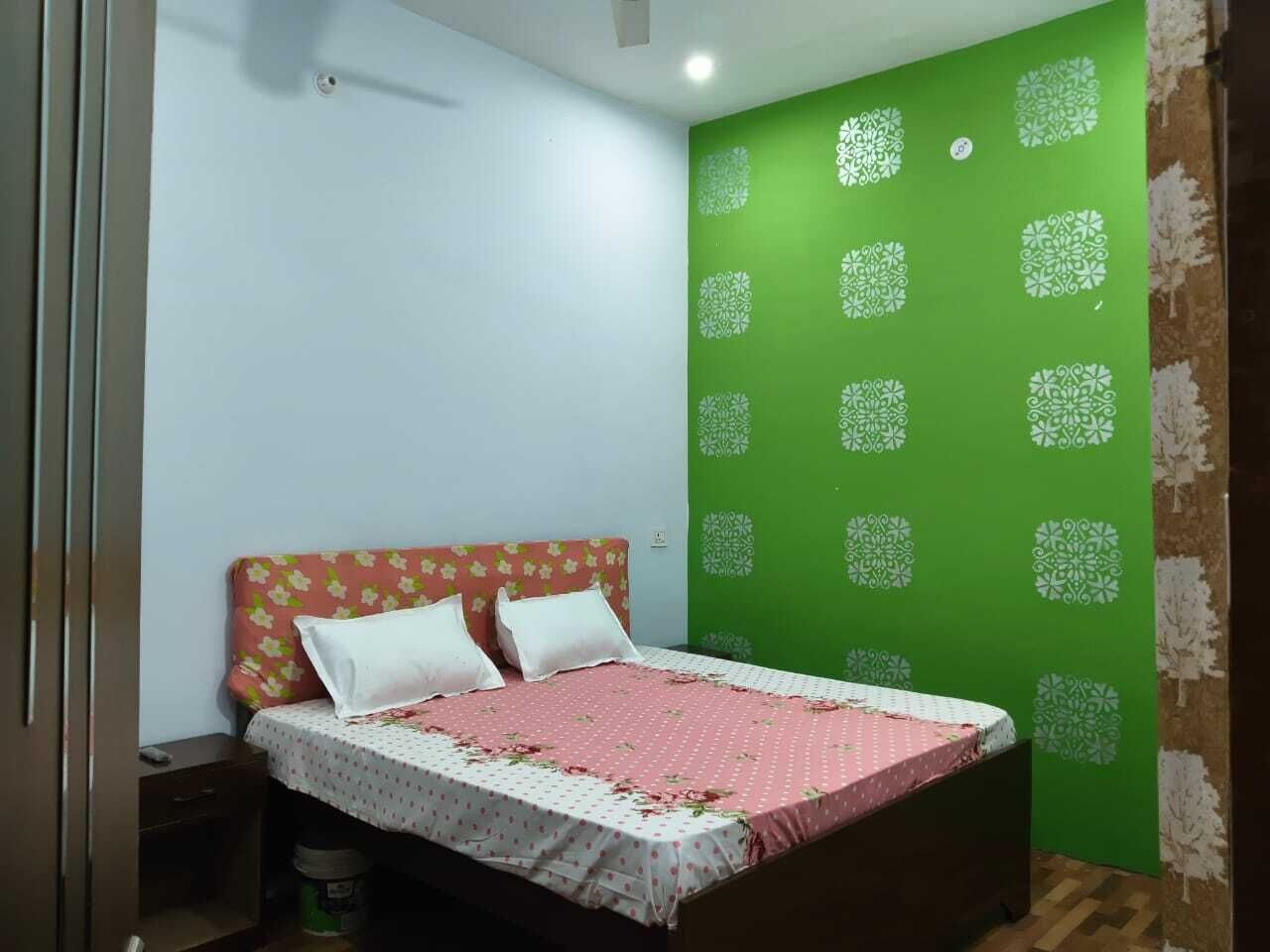 A bedroom with a bed, a nightstand, a green wall with a pattern, and a wooden floor.
