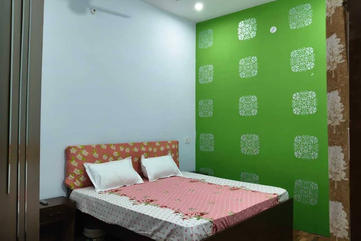Une chambre à coucher avec un lit, une table de chevet, un mur vert orné d’un motif et un plancher en bois.