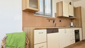 Una cocina con gabinetes de madera, lavavajillas, estufa y una ventana con persianas.