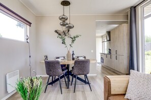 A modern dining area with a round table, two chairs, a decorative wall piece, and a view into the kitchen.