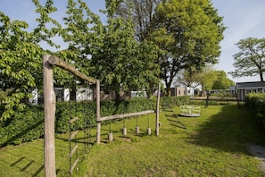 A playground with wooden climbing structures and swings, surrounded by lush green grass and trees.