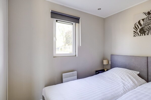 A bedroom with a bed, a nightstand with a lamp, a window with blinds, and a wall art piece.