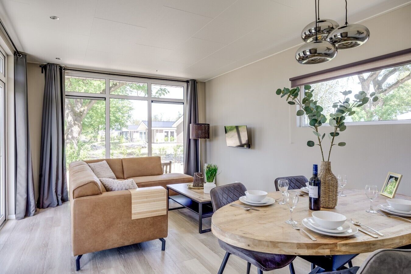 Un salon moderne avec un canapé, une table à manger et des chaises. Un téléviseur est fixé au mur et il y a une fenêtre avec des rideaux.
