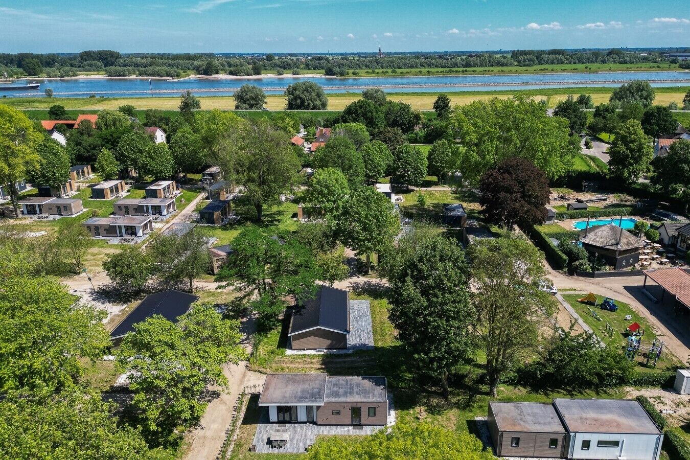 A residential area with houses, a swimming pool, and a river in the background.