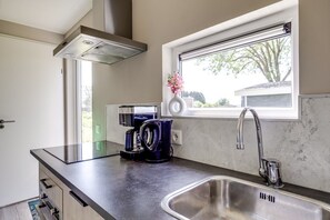 A kitchen with a stainless steel sink, a coffee maker, and a window with a view of trees.