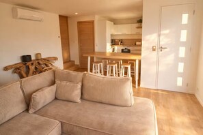 Ein Wohnzimmer mit einem beigen Sofa, einem Couchtisch aus Holz und einer Küche im Hintergrund.