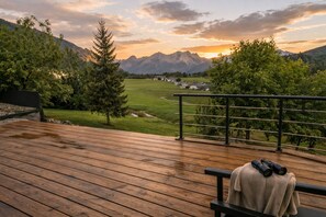 Eine Holzterrasse mit einer Bank, Fernglas und Handtuch mit Blick auf eine gebirgige Landschaft bei Sonnenuntergang.