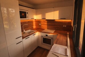 Eine kleine Küche mit weißen Schränken, einer Holzausziehtheke, einem eingebauten Ofen und einem Spülbecken.